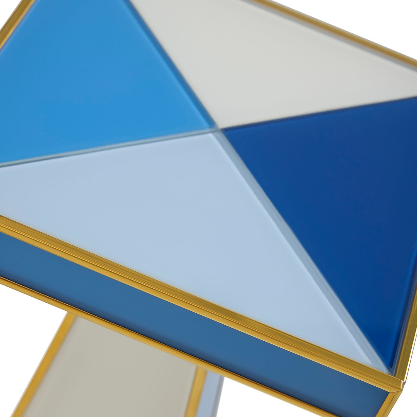 Close-up of a geometric side table top with triangular panels in blue, light blue, and white, framed by a gold metal border.
