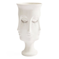 A white ceramic vase shaped like a stylized human face with closed eyes and small black speckled details under the eyes, shown on a plain white background.