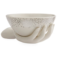 A white ceramic bowl with a dotted pattern on the exterior, displayed on a sculptural hand-shaped stand against a plain white background.