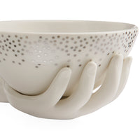 A white ceramic bowl with a perforated pattern of small dots on the exterior, supported by sculptural hand-shaped bases, shown against a plain white background.