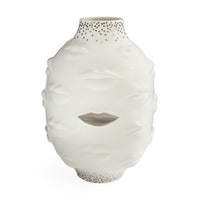 A white sculptural ceramic vase with a face-like relief design, featuring a cutout at the center of the mouth and small perforated dot details near the neck and base, shown on a plain white background.