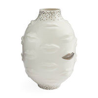 A white ceramic vase sculpted with a stylized face, featuring textured lips, closed eyes, and a metallic silver leaf detail on one eye. The neck and base are decorated with small metallic gold dots, set against a plain white background.